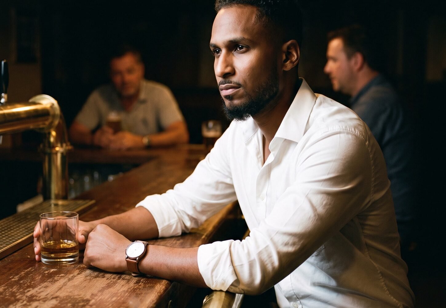 A man in a white shirt seated at a dimly lit bar, illustrating clothes and confidence.