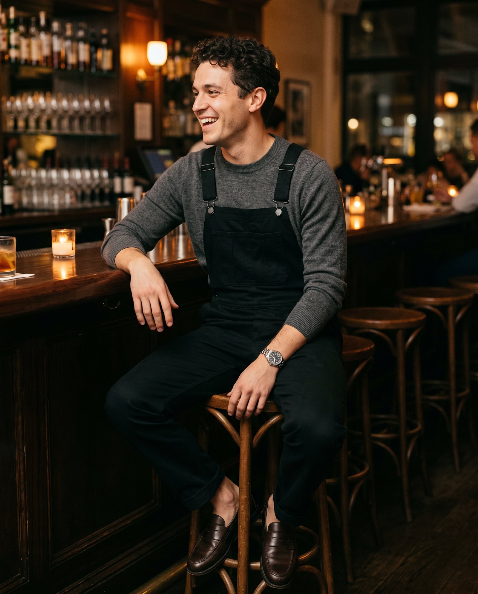 Young man in black overalls, a charcoal knit sweater and leather loafers at a restaurant bar