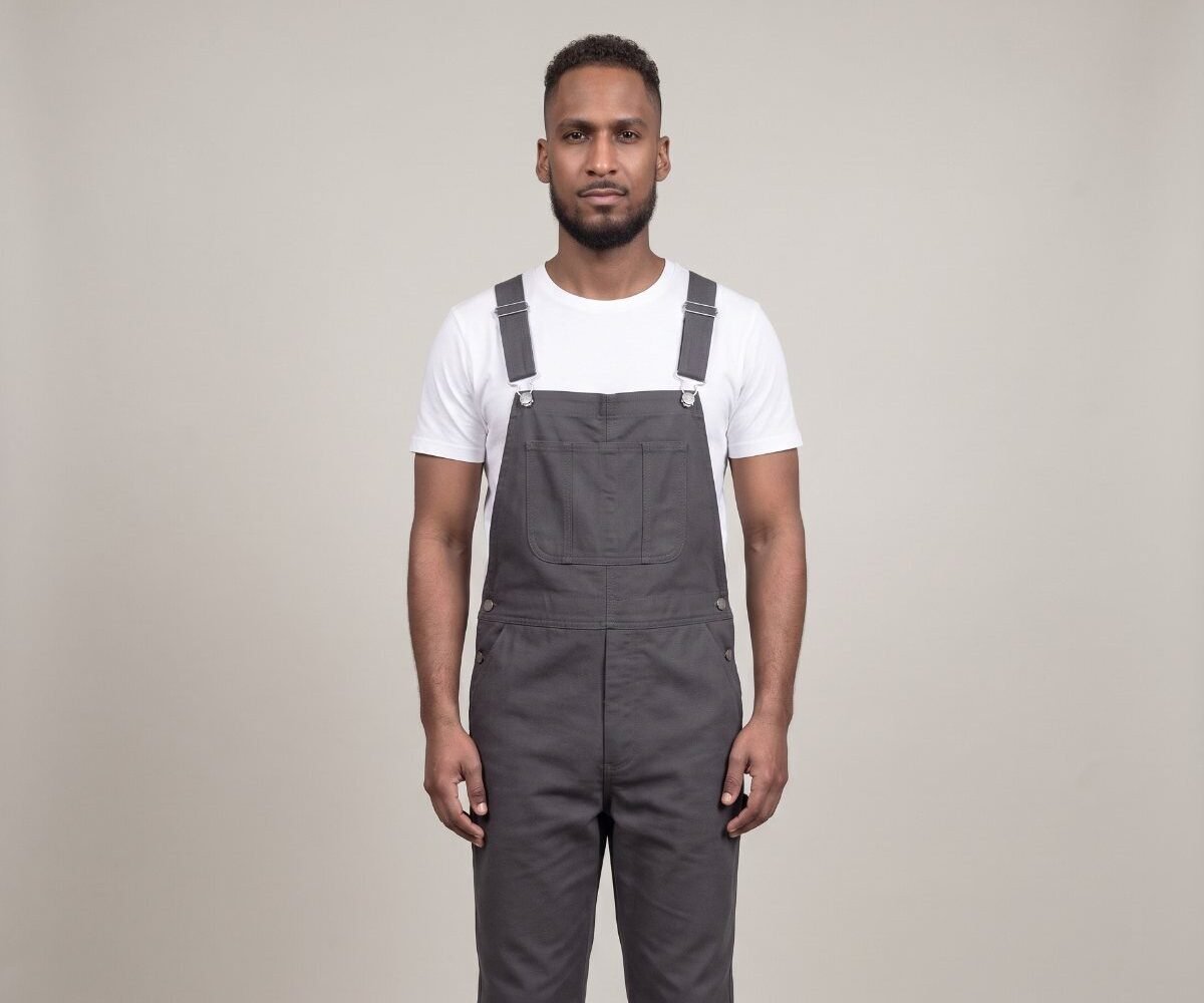 Front view of a man in well-fitted charcoal bib overalls over a white T-shirt, with the bib sitting at mid-chest