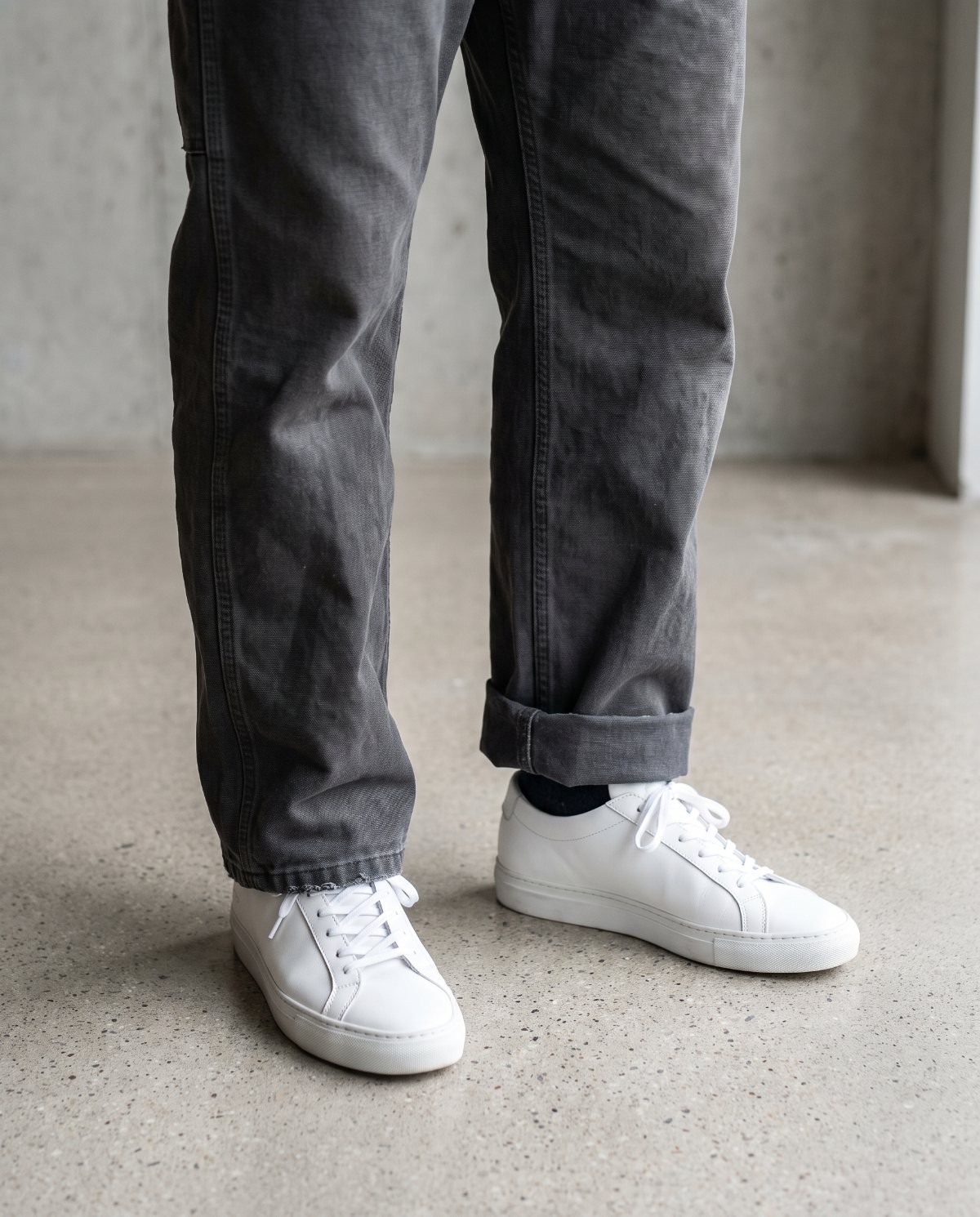 Charcoal overalls hems compared: one leg with a slight break over a white sneaker, the other with a single neat roll at the ankle