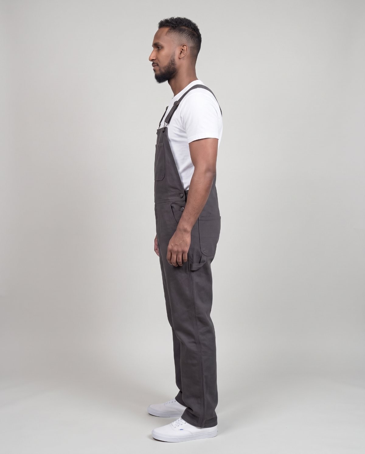 Side profile of a man in charcoal bib overalls showing strap angle, bib height and straight leg line